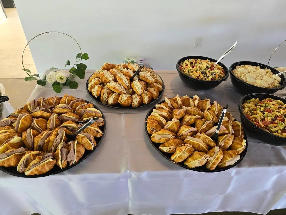 Wedding buffet table in white linen with platters of croissant sandwiches and pasta salad at an Akron reception