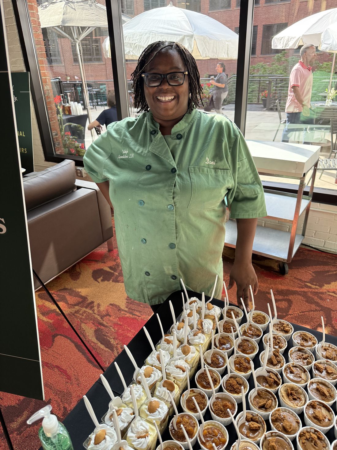 Danielle, owner of Tasteful Expectations, in a green chef coat behind a table of dessert cups at an Akron event