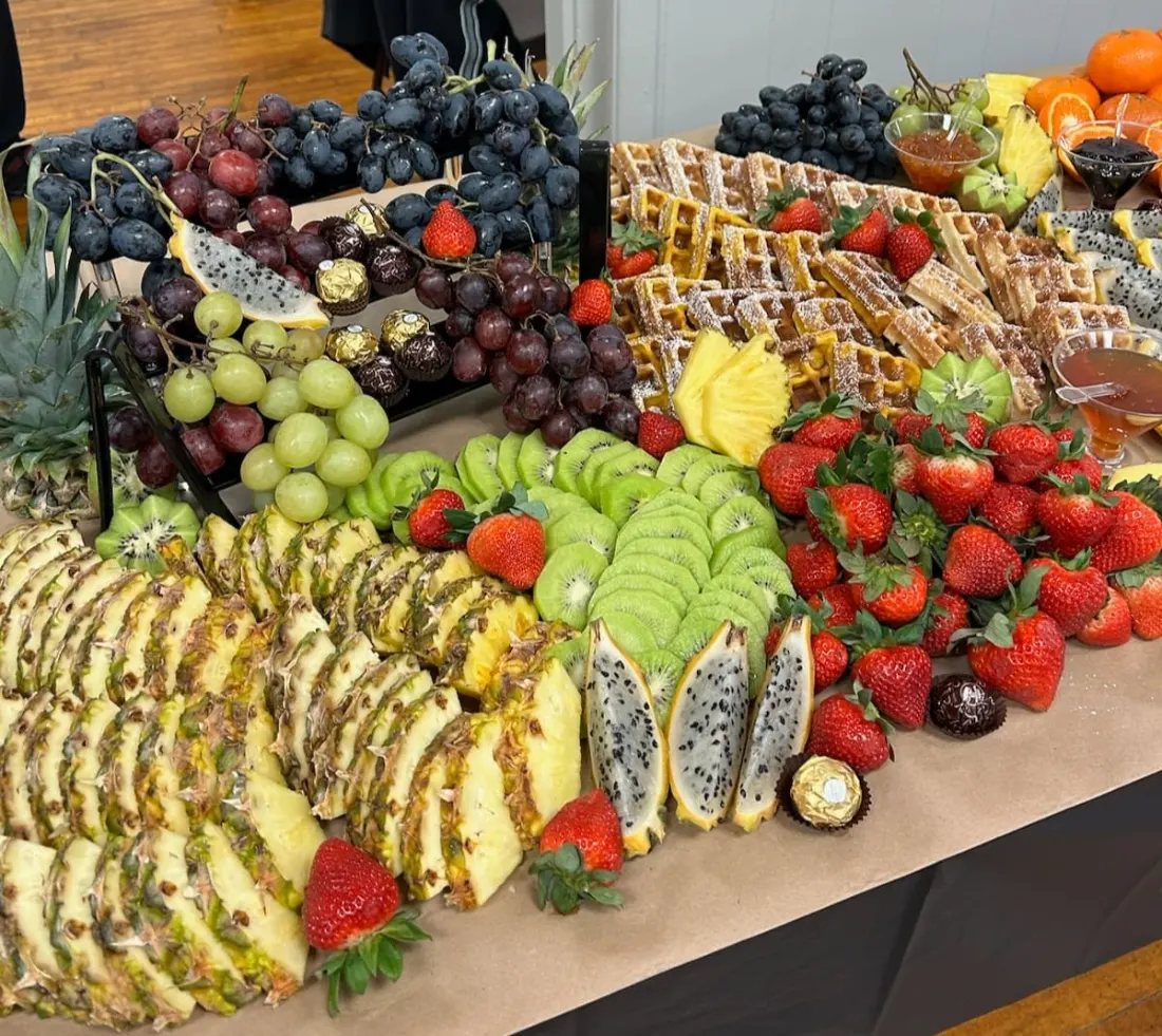 Fruit display of sliced pineapple, dragon fruit, grapes and strawberries arranged along a catering table