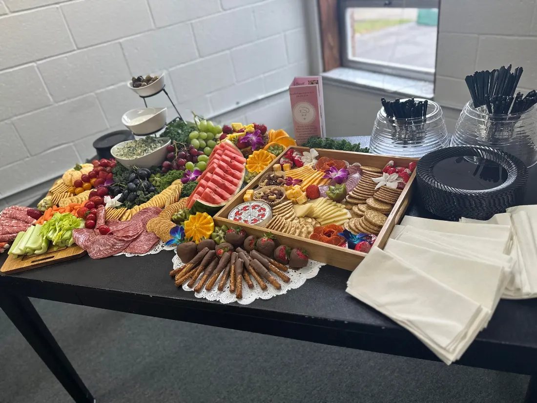 Long grazing table with a charcuterie board, cheeses and fruit on a black cloth at an Akron party