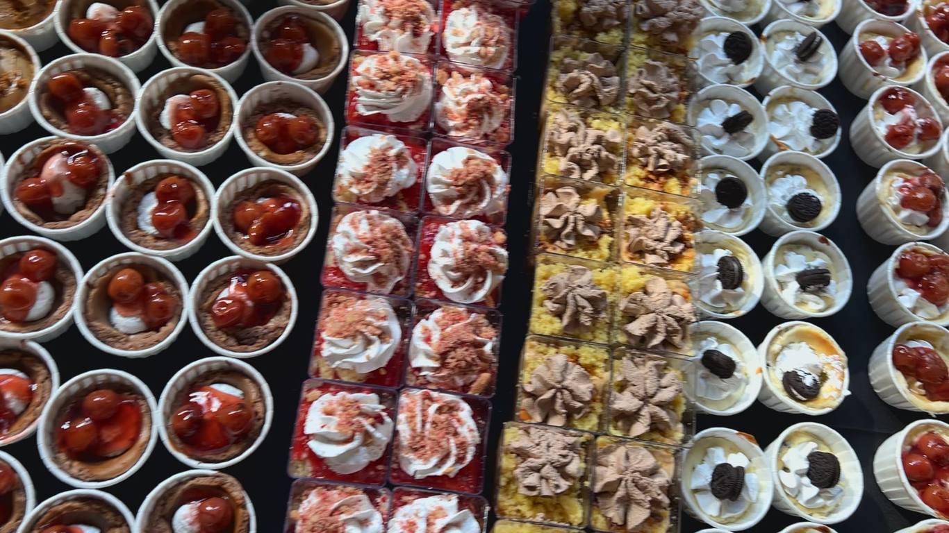 Overhead view of a catering dessert table filled with banana pudding cups, cherry cheesecake cups, brownies and lemon bars