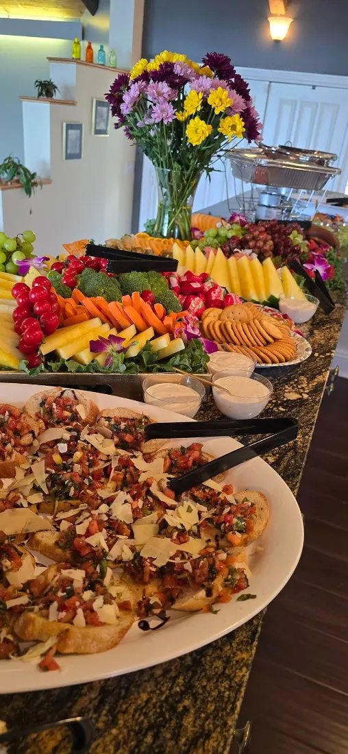 Fruit, cheese and appetizer platters on a serving table with a floral arrangement at a corporate reception